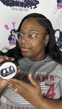 a black woman holding up a jar of hair powder